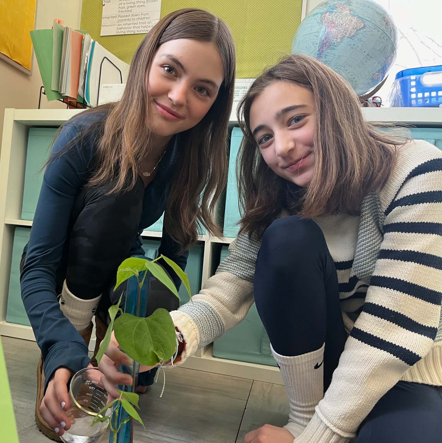 two girls smiling and displaying a plant