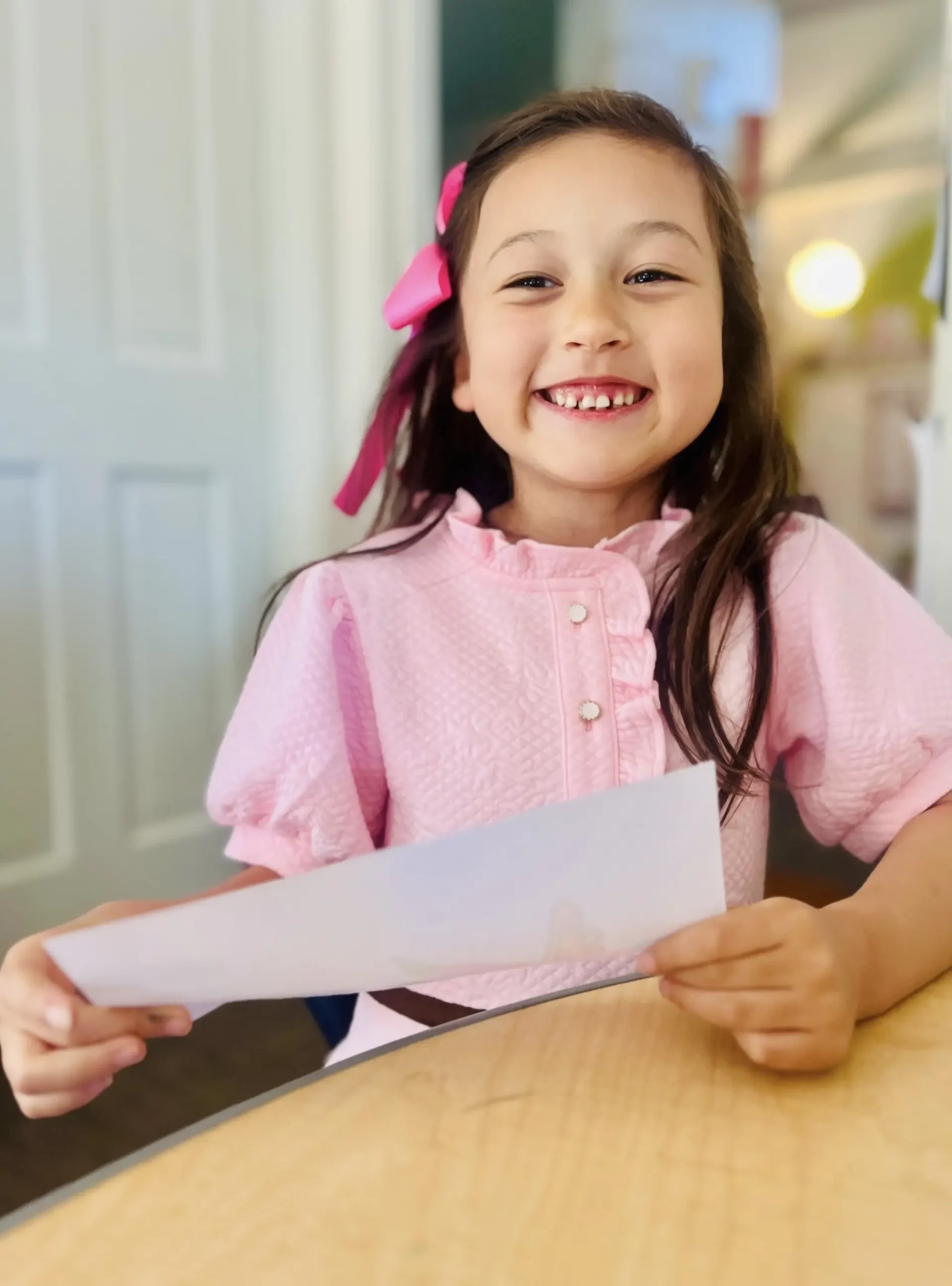 Young girl with a pink bow smiling, holding a white paper